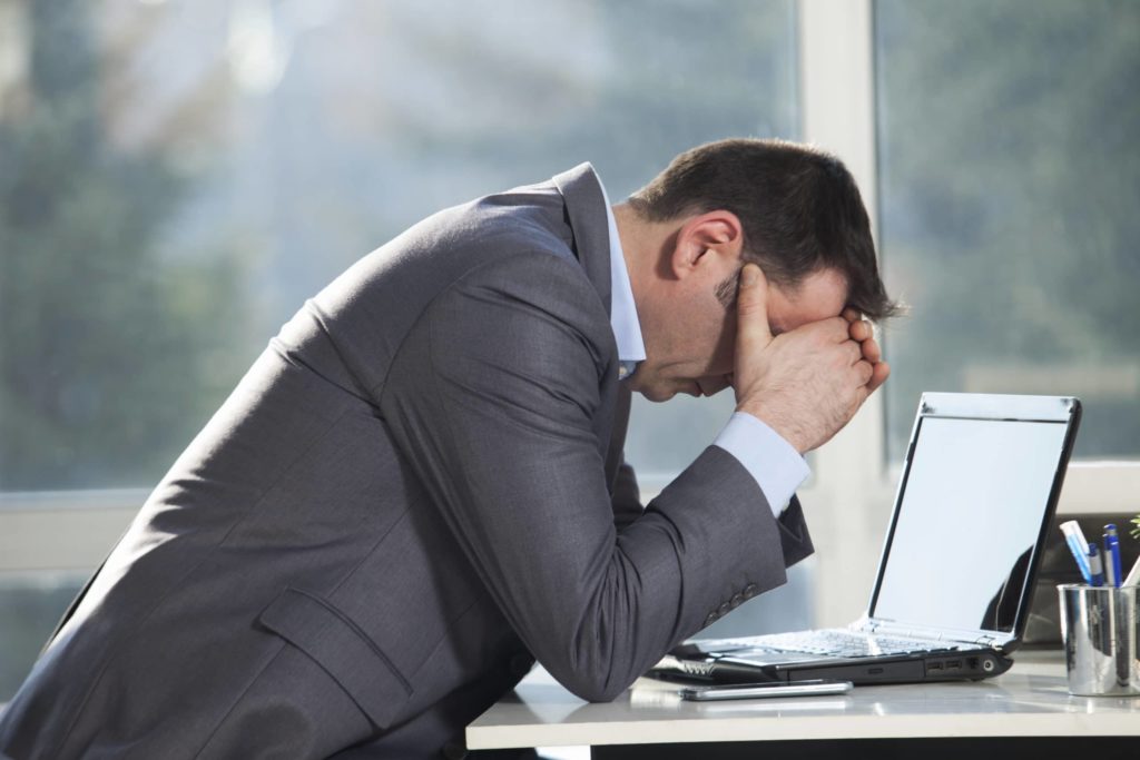man holding head in hands at desk